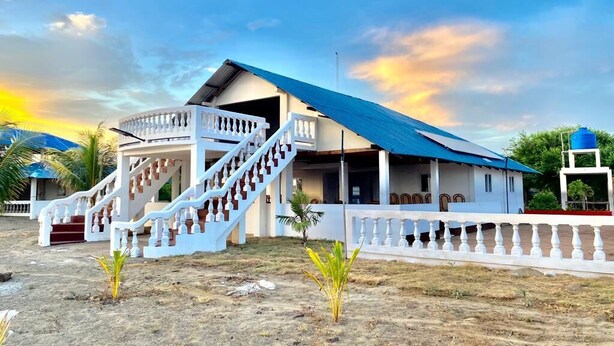 A building with a staircase leading to a covered porch, surrounded by a white fence and small plants. - Hostal Playa Azul (Corinto)