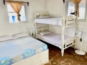 A bunk bed room with a single bed, a standing fan, and a window with curtains.