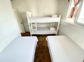 A small, compact room with two single beds, a window with curtains, and a door.