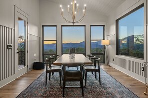 Ein Essbereich mit großem Tisch, Stühlen, einer Deckenleuchter und Bergblick durch große Fenster.