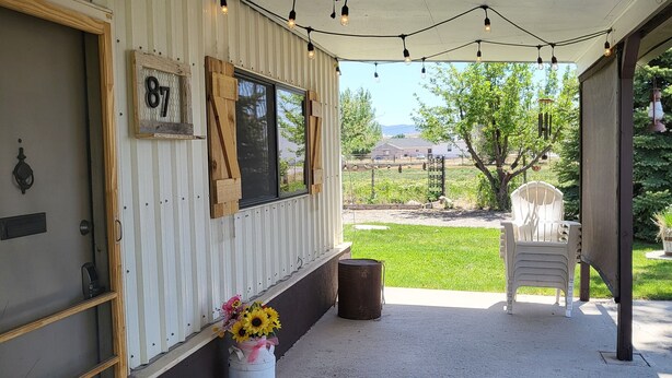 A covered porch with string lights, a wooden door with a number sign, a window, and a chair outside.