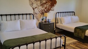A bedroom with two beds, a ceiling fan, a nightstand with a lamp, and a large cow skull mounted on the wall.