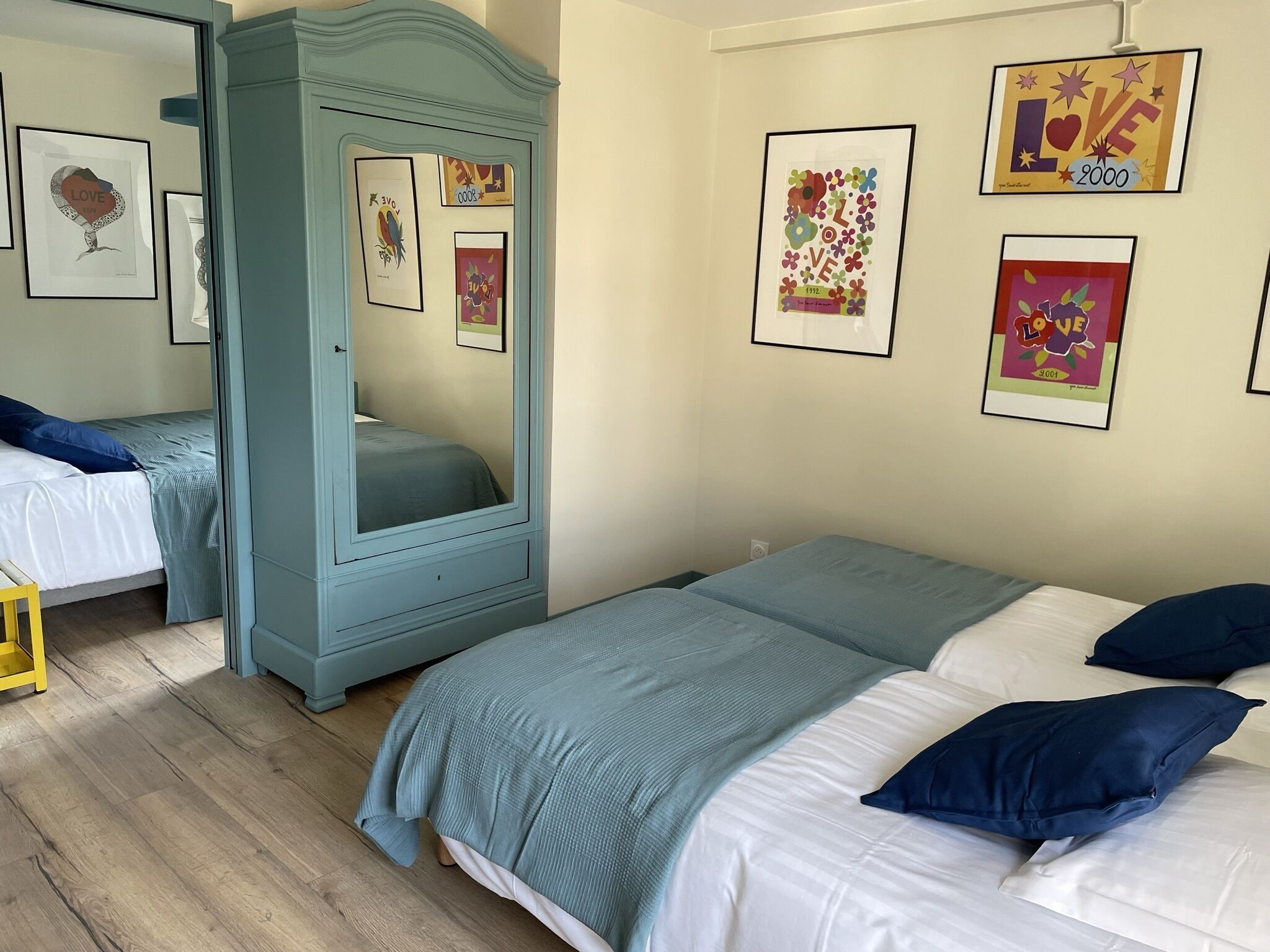Une chambre avec deux lits, une armoire et plusieurs œuvres d’art encadrées accrochées au mur.