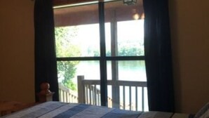 A room with a large bed, a window with curtains, and a view of greenery outside. - Beautiful Secluded Cabin on the White River (Calico Rock)