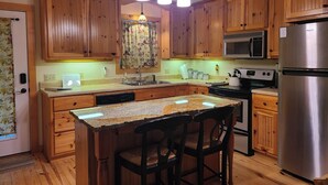 A kitchen with wooden cabinets, a granite countertop, a stainless steel refrigerator, and a microwave. - Beautiful Secluded Cabin on the White River (Calico Rock)