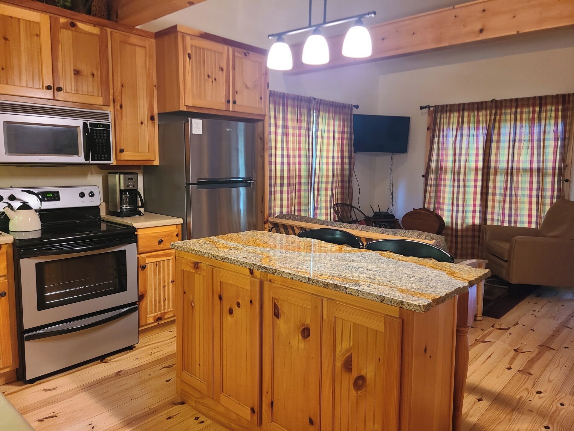 A kitchen with wooden cabinets, a stainless steel refrigerator, a microwave, an oven, and a granite countertop.