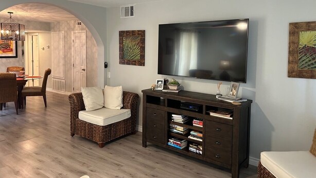 A living room with a dark wood entertainment center, a flat-screen TV, and a dining area with wicker furniture.