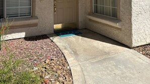 A stucco house with a front door, a window with a metal grill, and a small porch area.
