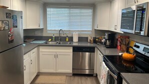 A modern kitchen with white cabinetry, stainless steel appliances, a dishwasher, and a window with blinds.