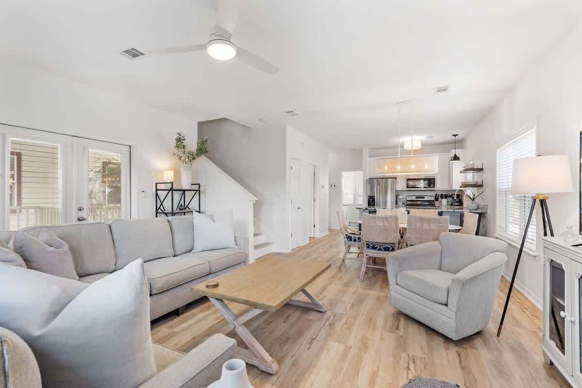 A spacious living room with a sofa, armchairs, and a coffee table. A staircase leads to a kitchen area with modern appliances.