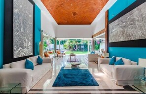 Relax in this stylish living room with a glass coffee table, two sofas, and a unique ceiling design, offering a view of the beautiful garden.