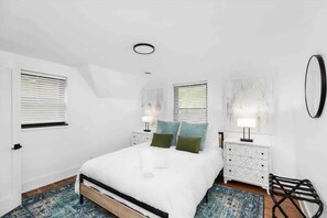 A bedroom with a bed, two bedside tables, a wall-mounted mirror, and a patterned rug. - 5BR Detroit Mansion | Sleeps 16 | Driveway Parking (Detroit)