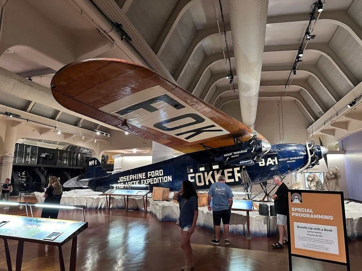 An airplane exhibit with a visible cockpit, a person standing near the aircraft, and informational signage.