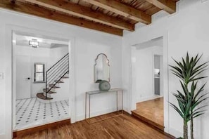 Un pasillo con suelo de madera, una escalera, una consola con espejo y una planta en maceta.