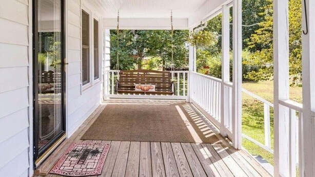Un portico riparato con una panca di legno, un tappetino d'ingresso e vista su un giardino.