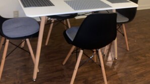 Un'area pranzo con un tavolo bianco, quattro sedie nere e un laptop sul tavolo.