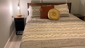 Ein ordentlich bezogenes Bett mit gemusterten Betttextilien, einer Nachttischlampe und einem Holznachttisch.