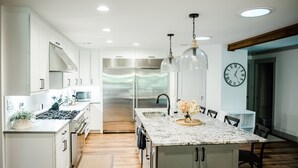 Una cocina moderna con armarios blancos, un refrigerador de acero inoxidable, una isla de mármol y luces colgantes.