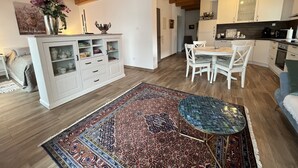 A modern kitchen with white cabinets, a dining area with a round table and chairs, and a large patterned rug on the floor. - Wohnung Carmen (Bad Rappenau)