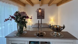 A room with a wooden ceiling, a bed with a white headboard, a bedside table with a lamp, a vase with flowers, and a silver bowl on a tray. - Wohnung Carmen (Bad Rappenau)
