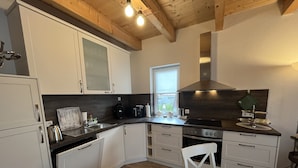 A modern kitchen with white cabinets, a black countertop, and a wooden ceiling. - Wohnung Carmen (Bad Rappenau)