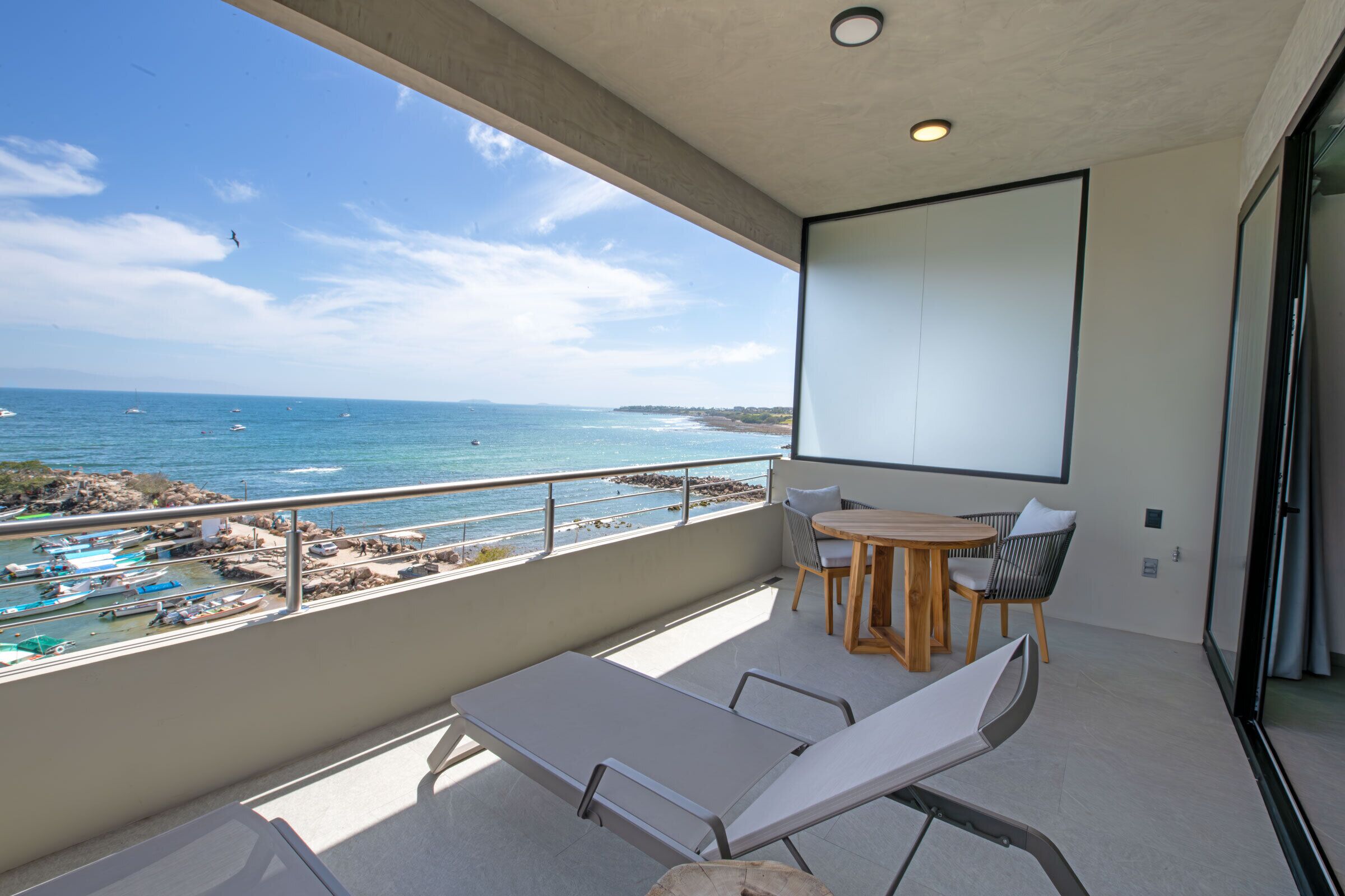 Uma varanda com vista para o mar, uma mesa com cadeiras e uma tela de projeção.