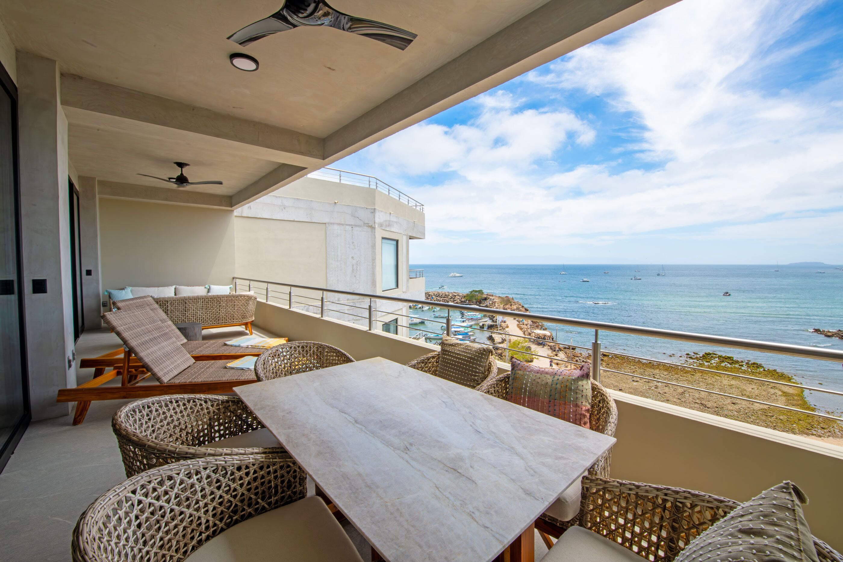 Un balcone con mobili in vimini, un tavolo e vista sul mare.