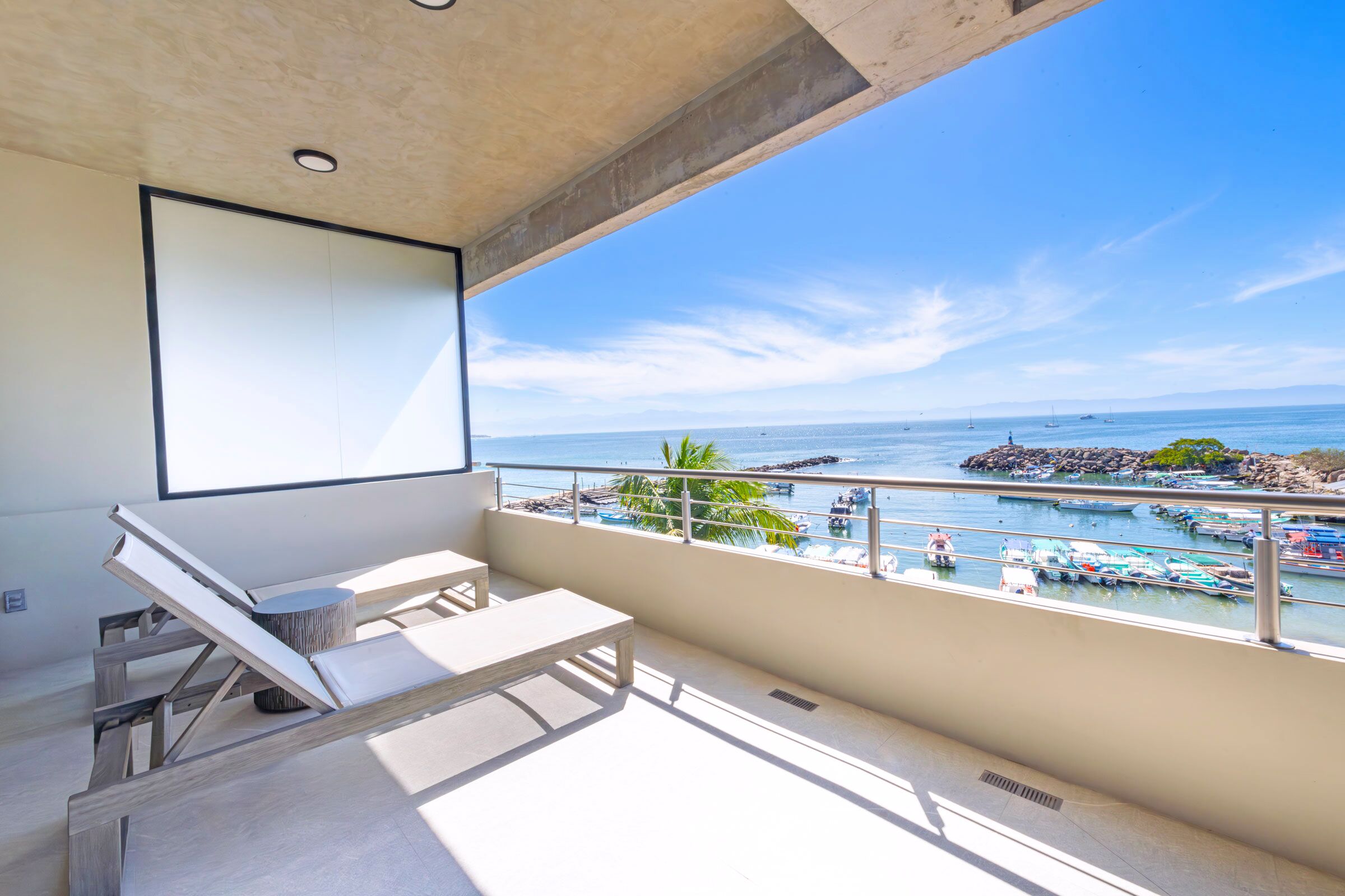 A balcony with a view of the sea, a lounge chair, and a small table.