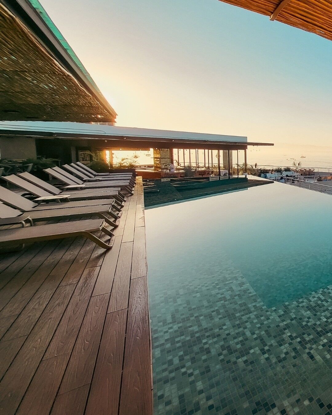 Un espace aménagé au bord de la piscine, avec des chaises longues, une terrasse en bois et une vue sur la mer.