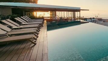 Un espace aménagé au bord de la piscine, avec des chaises longues, une terrasse en bois et une vue sur la mer.