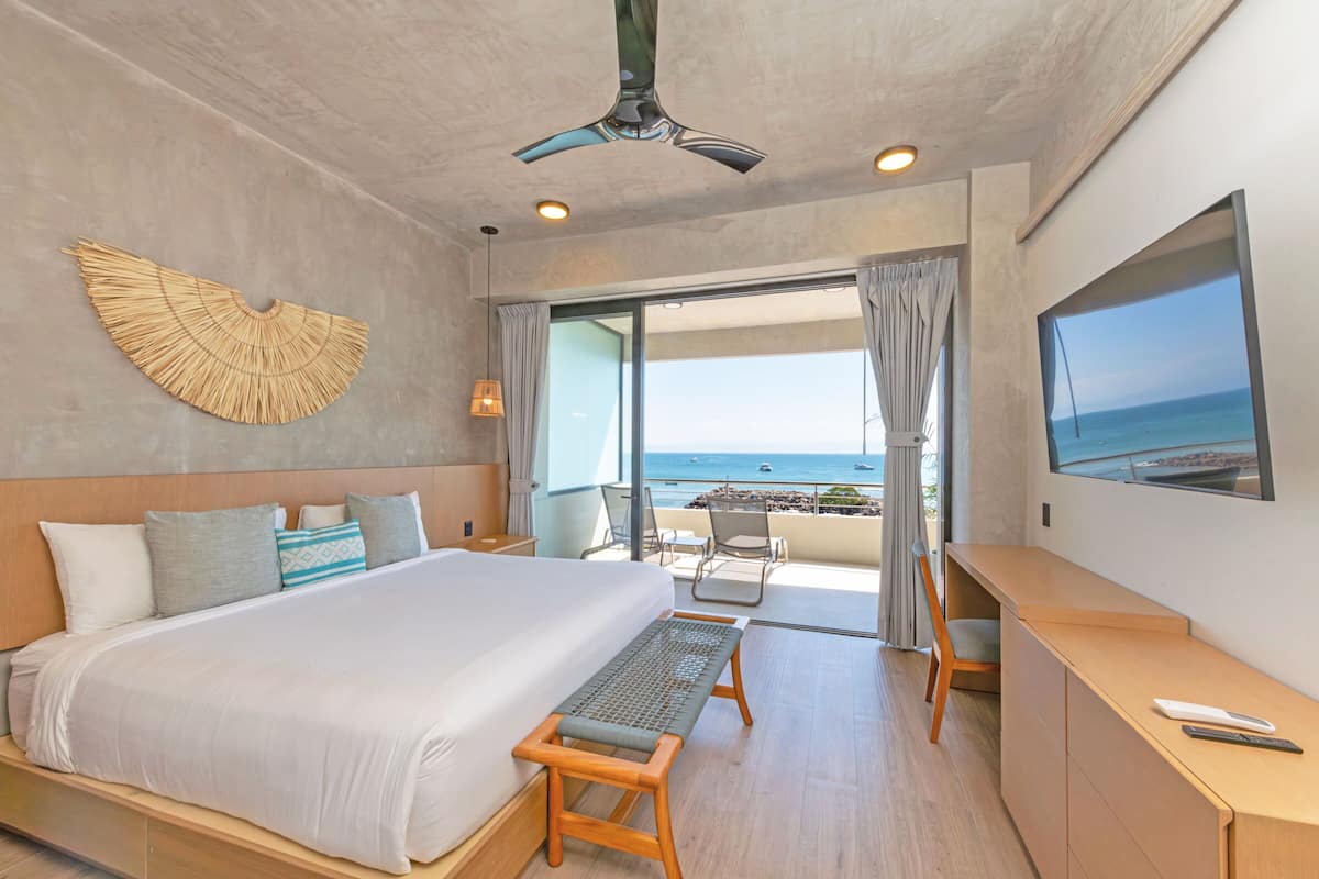 Una habitación de hotel moderna con una cama grande, un escritorio, una silla y vistas al mar.