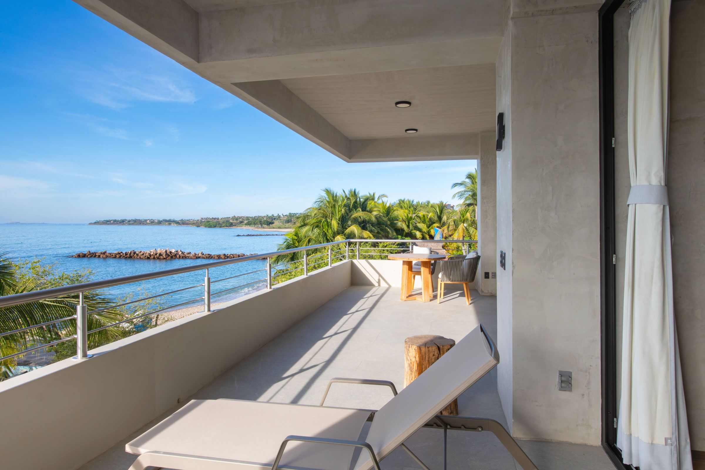 Un balcón con vista al mar, una mesa con sillas y un taburete de madera.