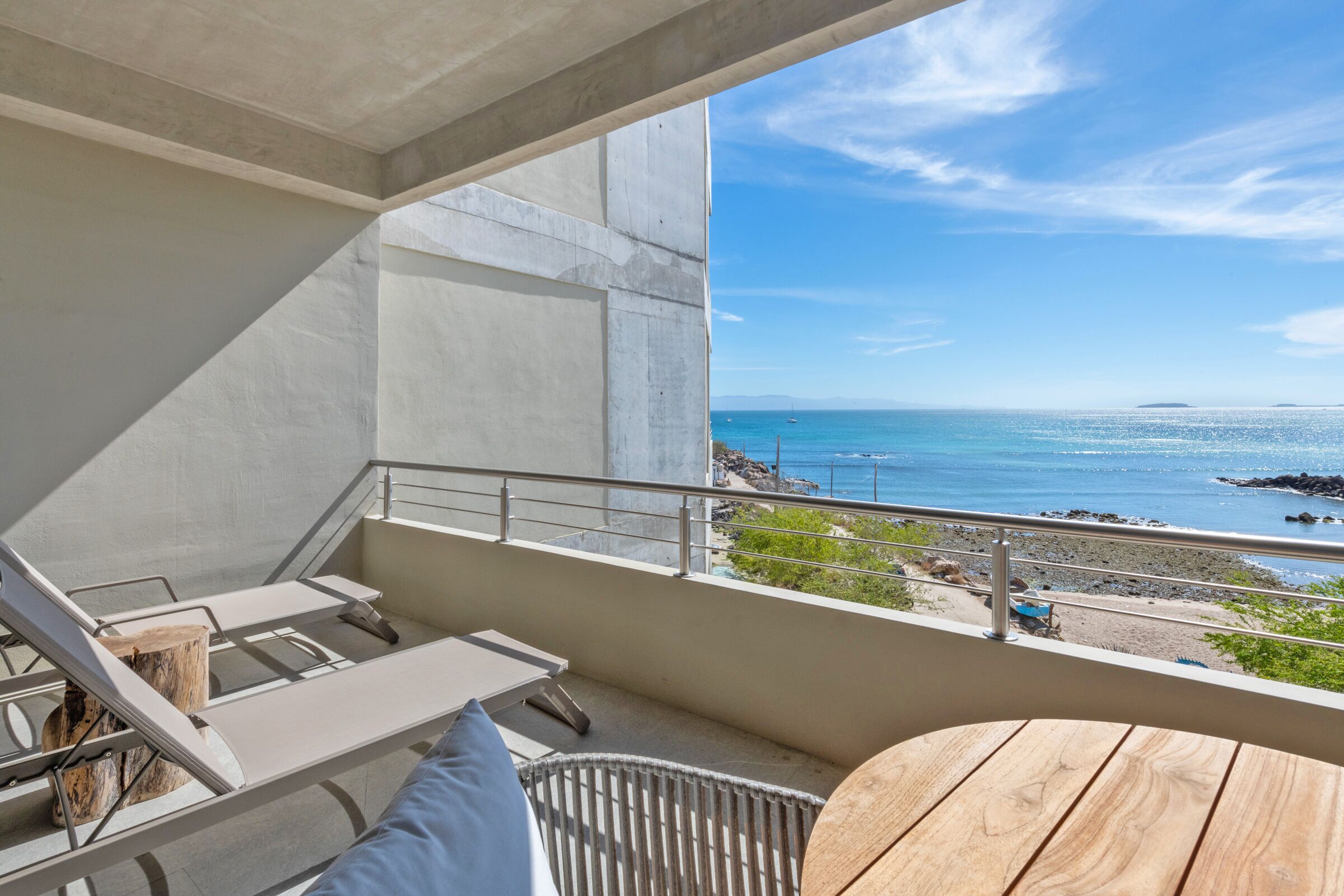 A balcony with a view of the sea, a wooden table, and lounge chairs.