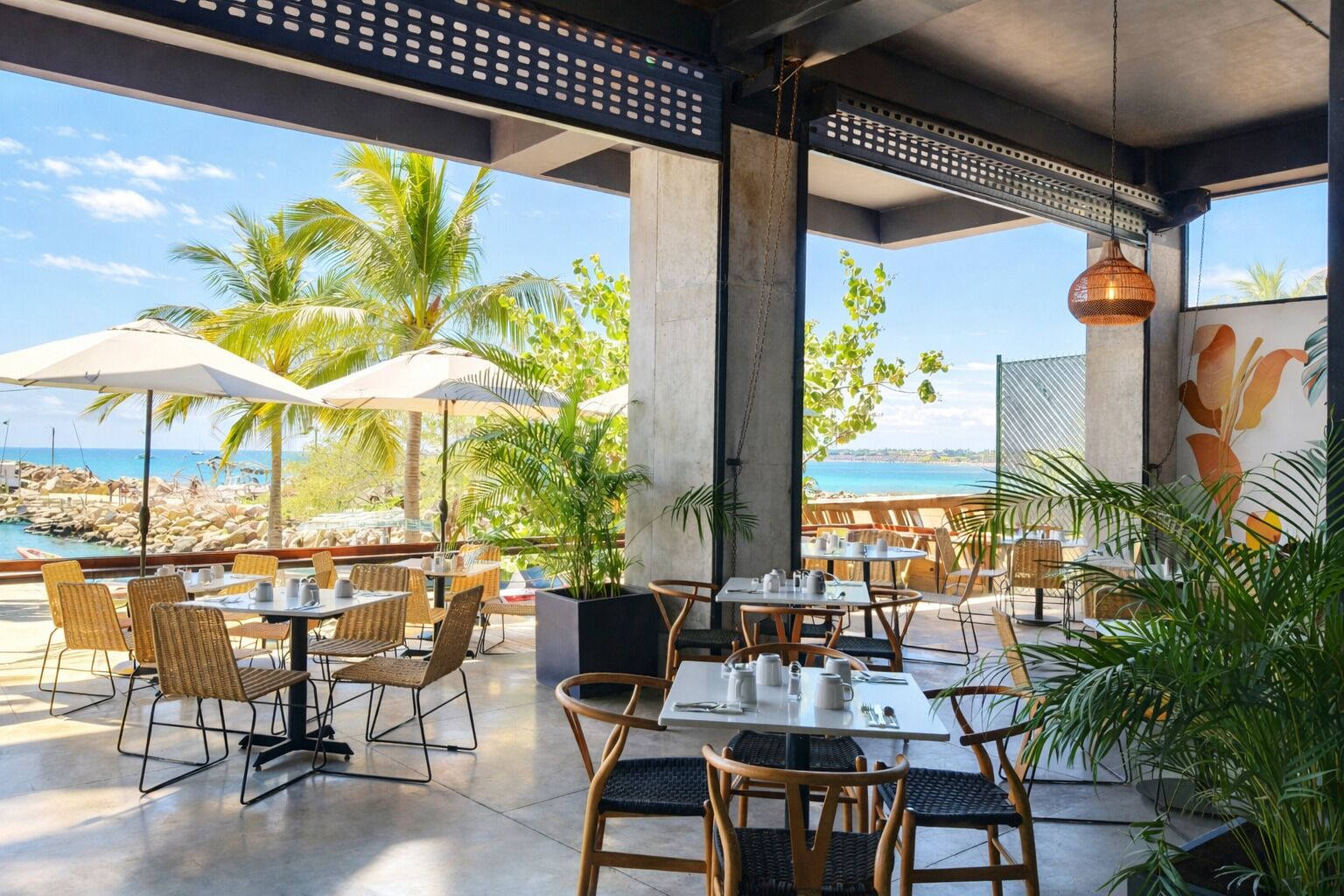An outdoor dining area with tables and chairs, large umbrellas, and a view of the beach and ocean.