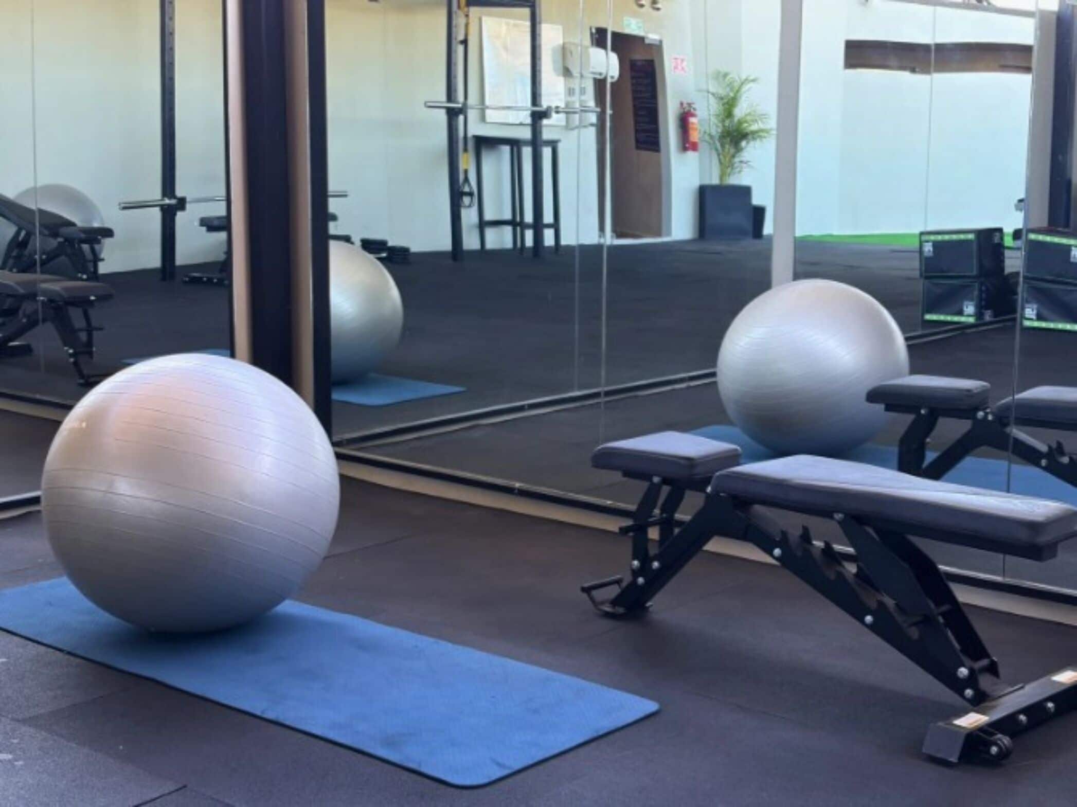 Un gimnasio con pelotas de ejercicio, bancos y un espejo que refleja el espacio.