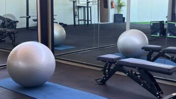 Un gimnasio con pelotas de ejercicio, bancos y un espejo que refleja el espacio.