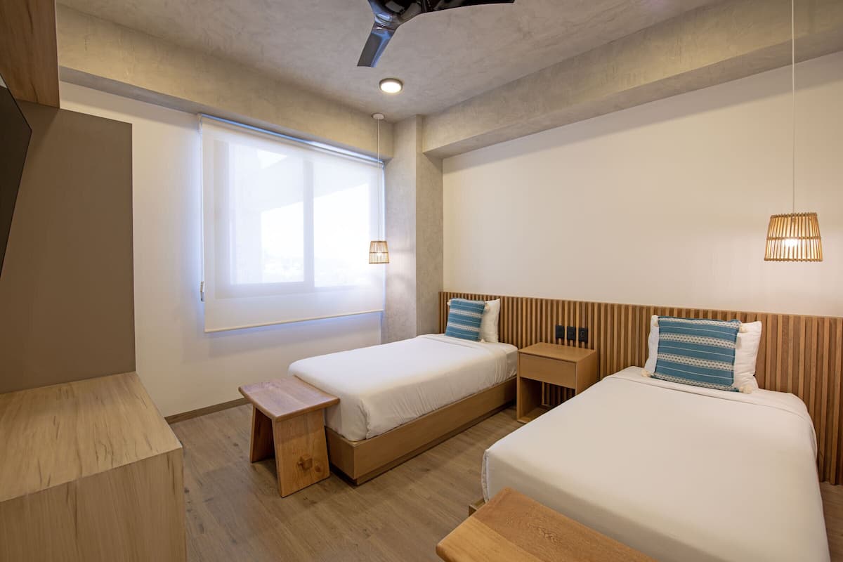 Un dormitorio moderno con dos camas individuales, una mesita de noche de madera, una pequeña mesa de madera y una ventana con persianas.