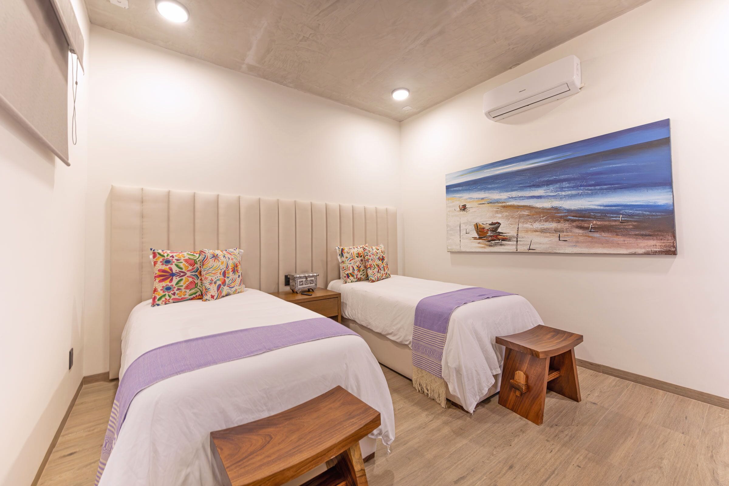 A hotel room with two beds, a painting on the wall, and a wooden bench.