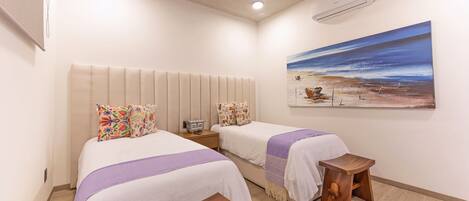 A hotel room with two beds, a painting on the wall, and a wooden bench.