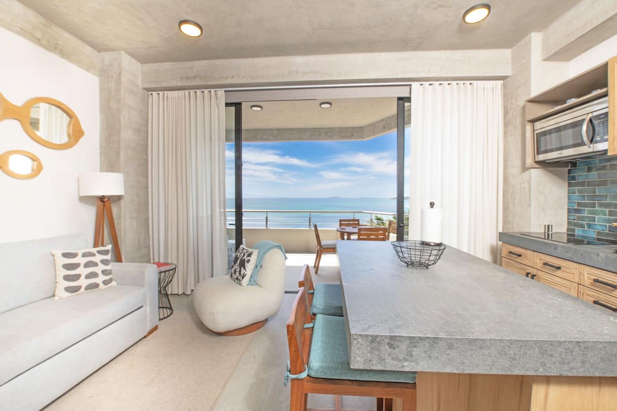 Una cocina moderna con una isla grande, un comedor con vistas y una zona de estar acogedora con vista al océano.