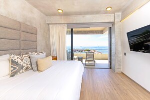 Habitación de hotel moderna con una cama grande, un balcón con vista al mar y un televisor de pantalla plana montado en la pared.
