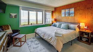 A bedroom with a large bed, a wooden headboard, a nightstand with a lamp, a green wall, and a window with a view. - Hike, Ski & Fish! Sunset-View Condo in Beech Mtn (Beech Mountain)