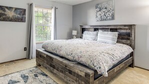Een slaapkamer met een houten bedframe, een raam met gordijnen en een bloemschilderij aan de muur.
