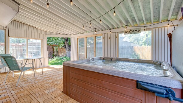 Een hottub in een overdekte patio met houten vloer, een tafel en stoelen.