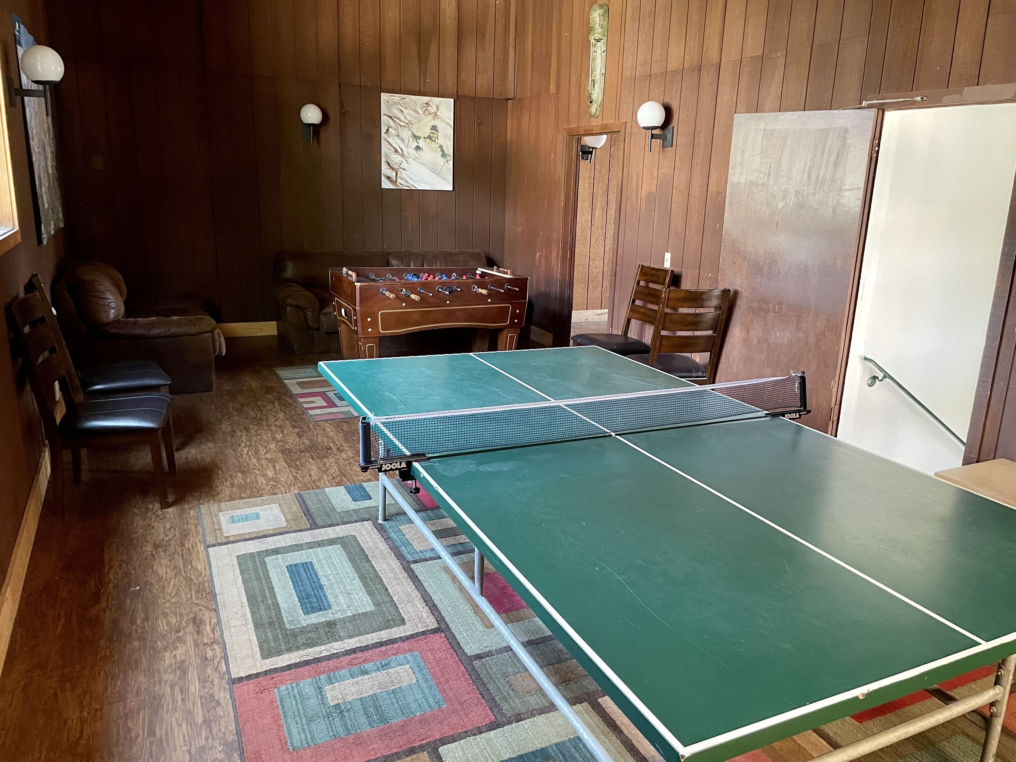 Una habitación con mesa de ping pong, mesa de futbolín, sofá y refrigerador.