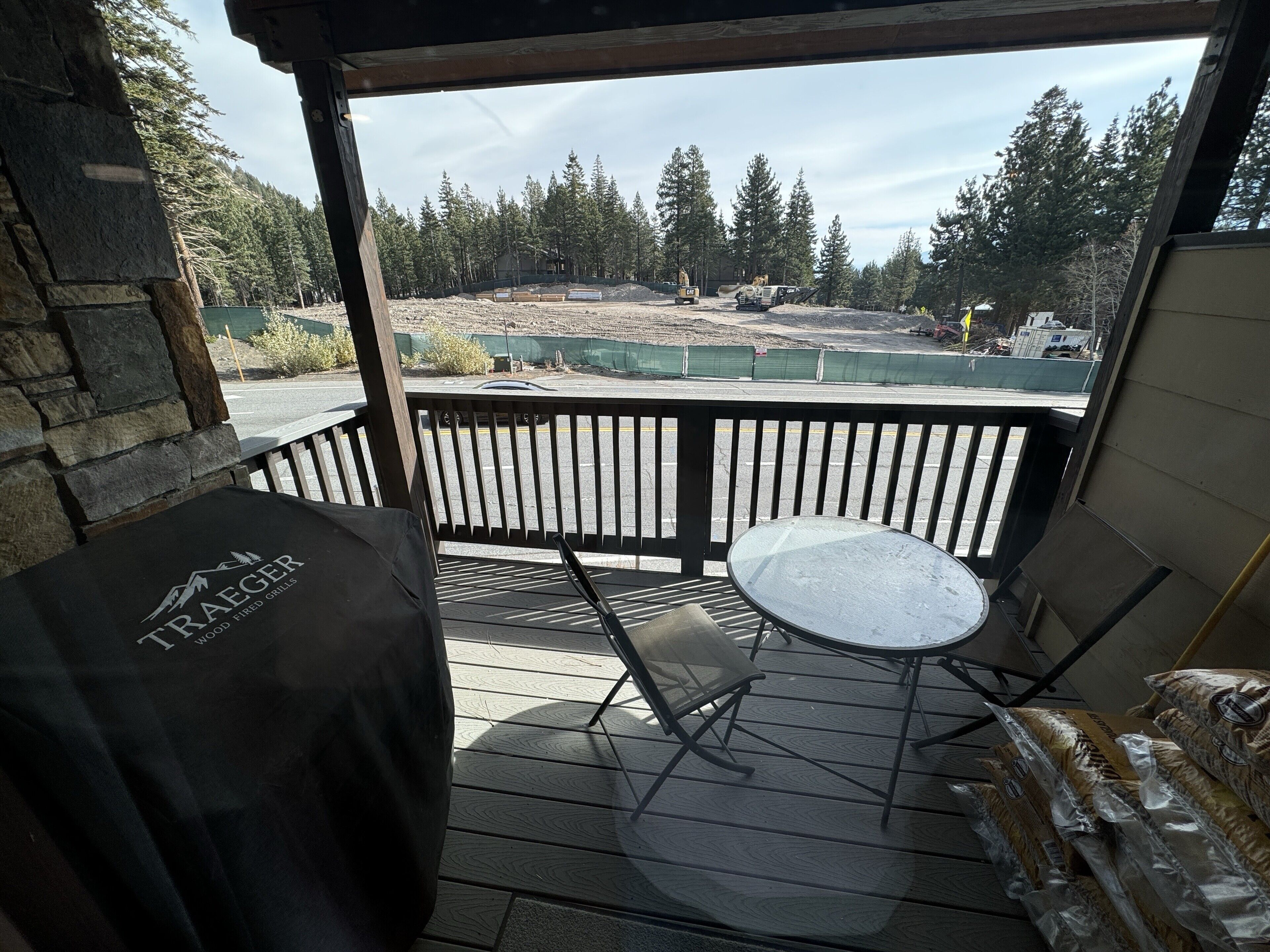 A covered outdoor area with a table and chairs, a grill, and a view of a construction site and forest.