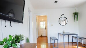 Un salón moderno con un televisor de pantalla plana, suelo de madera, una mesa de comedor y varias plantas en macetas.