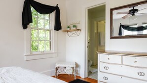 Un dormitorio con cama, cómoda, ventana con cortinas, una mesita y un espejo.
