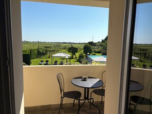 Un balcón con mesa y sillas, vista a un viñedo y una piscina.