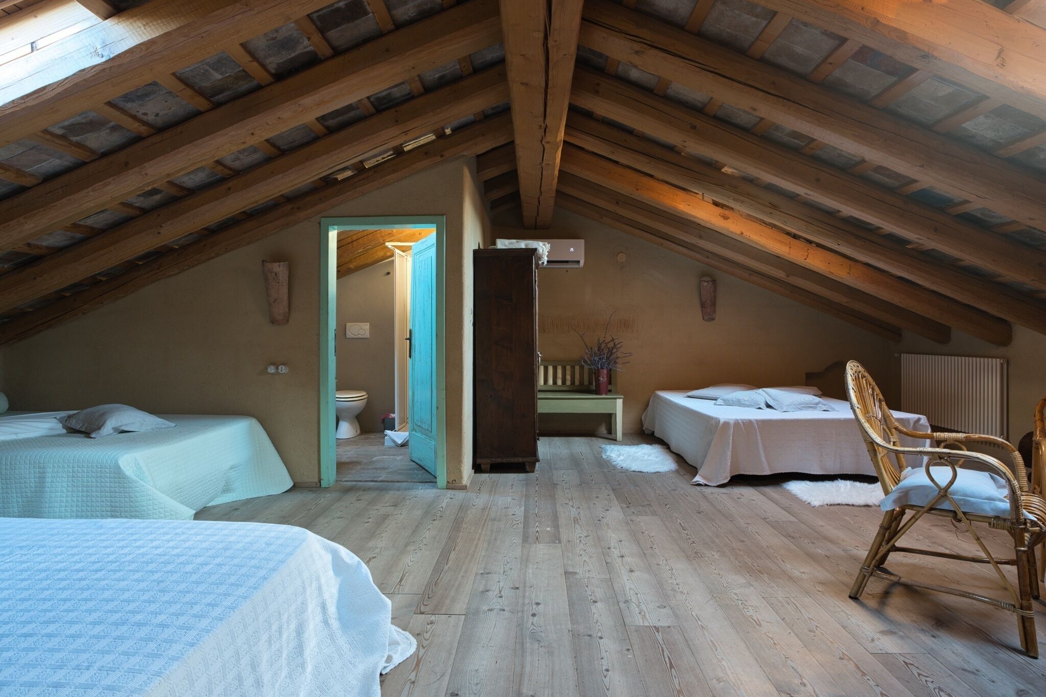Un dormitorio acogedor en el ático, con vigas de madera, dos camas, una silla y una mesita.